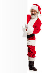 Image showing Happy Santa Claus pointing on blank advertisement banner background with copy space. Smiling Santa Claus pointing in white blank sign