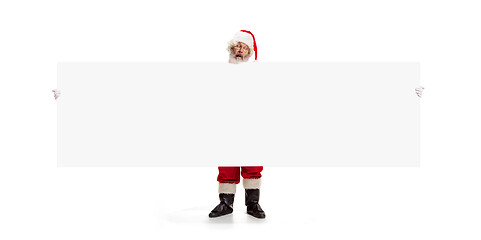 Image showing Happy Santa Claus pointing on blank advertisement banner background with copy space. Smiling Santa Claus pointing in white blank sign