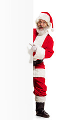 Image showing Happy Santa Claus pointing on blank advertisement banner background with copy space. Smiling Santa Claus pointing in white blank sign