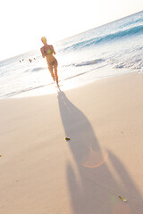 Image showing Happy woman enjoying in summer, running joyfully on tropical beach in sunset. Beautiful caucasian model wearing bikini on vacations on sandy beach. Footprints in sand. Copy space