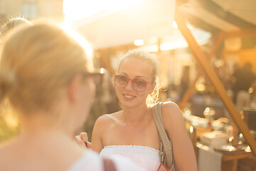 Image showing It is nice to see you. It has been a while. Two happy young female friends enjoying a conversation on urban food market at random after work encounter. Pleasant free time socializing