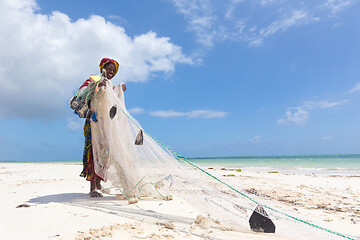 Image showing Traditional african local rural fishing on Paje beach, Zanzibar, Tanzania. Traditionally dressed local woman pulling fishing net, catching small fish.