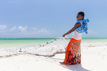 Image showing Traditional african local rural fishing on Paje beach, Zanzibar, Tanzania. Traditionally dressed local woman pulling fishing net, catching small fish.