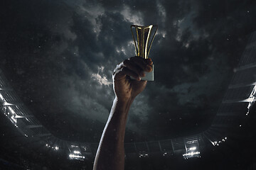 Image showing Award of victory, male hands tightening the cup of winners against cloudy dark sky