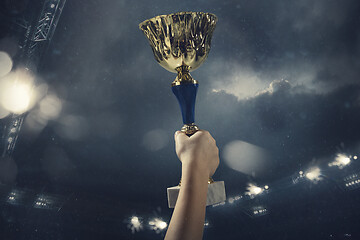 Image showing Award of victory, male hands tightening the cup of winners against cloudy dark sky