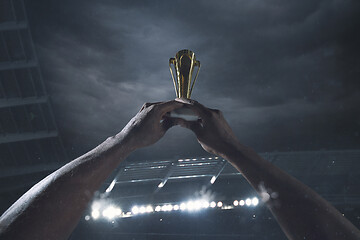 Image showing Award of victory, male hands tightening the cup of winners against cloudy dark sky