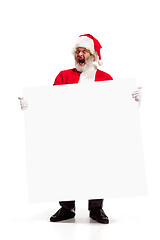 Image showing Happy Santa Claus pointing on blank advertisement banner background with copy space. Smiling Santa Claus pointing in white blank sign