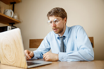 Image showing Feeling sick and tired. Frustrated young man massaging his head while sitting at his working place in office