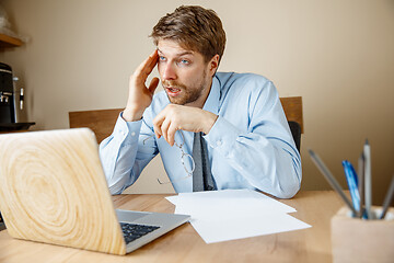 Image showing Feeling sick and tired. Frustrated young man massaging his head while sitting at his working place in office