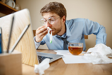 Image showing Sick man while working in office, businessman caught cold, seasonal flu.