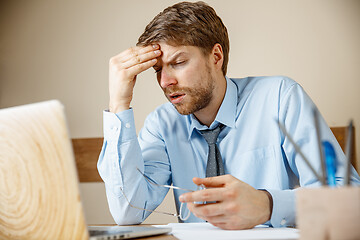 Image showing Feeling sick and tired. Frustrated young man massaging his head while sitting at his working place in office