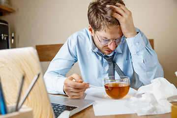 Image showing Feeling sick and tired. Frustrated young man massaging his head while sitting at his working place in office