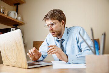 Image showing Feeling sick and tired. Frustrated young man massaging his head while sitting at his working place in office