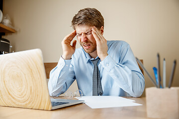 Image showing Feeling sick and tired. Frustrated young man massaging his head while sitting at his working place in office