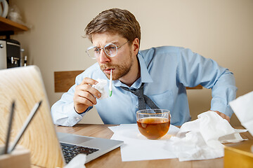 Image showing Sick man while working in office, businessman caught cold, seasonal flu.