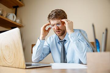 Image showing Feeling sick and tired. Frustrated young man massaging his head while sitting at his working place in office