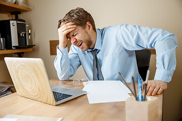 Image showing Feeling sick and tired. Frustrated young man massaging his head while sitting at his working place in office