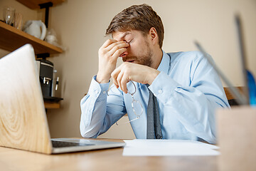 Image showing Feeling sick and tired. Frustrated young man massaging his head while sitting at his working place in office