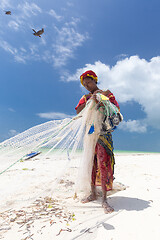Image showing Traditional african local rural fishing on Paje beach, Zanzibar, Tanzania. Traditionally dressed local woman pulling fishing net, catching small fish.