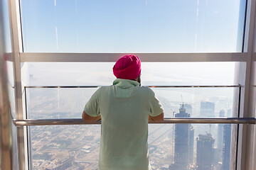 Image showing Indian sikh man wearing traditional colorfu turban, admiring city view from modern observing platform at top of the tallest skyscraper in the world, Burj Khalifa in Dubai, UAE.