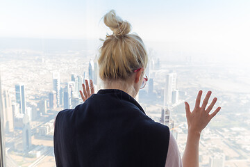 Image showing Beautiful girl admiring the city view from observing platform at the top of the tallest skyscraper in the world, Burj Khalifa in Dubai, UAE.