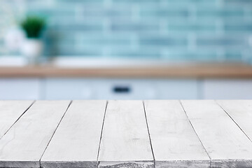 Image showing Empty white wooden boards or table top over blurred kitchen interior on background. Template, mockup for display or montage. Close up, copy space