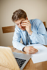 Image showing Feeling sick and tired. Frustrated young man massaging his head while sitting at his working place in office