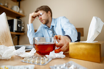 Image showing Feeling sick and tired. Frustrated young man massaging his head while sitting at his working place in office