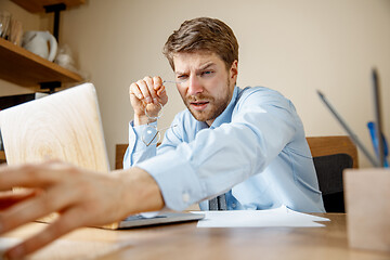 Image showing Feeling sick and tired. Frustrated young man massaging his head while sitting at his working place in office