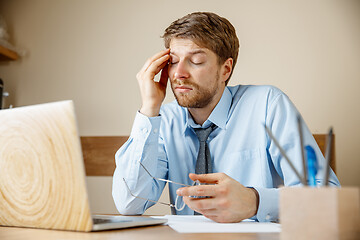 Image showing Feeling sick and tired. Frustrated young man massaging his head while sitting at his working place in office