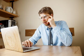 Image showing Feeling sick and tired. Frustrated young man massaging his head while sitting at his working place in office