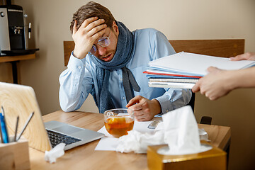 Image showing Feeling sick and tired. Frustrated young man massaging his head while sitting at his working place in office