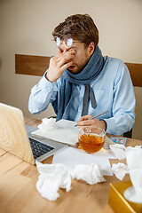 Image showing Feeling sick and tired. Frustrated young man massaging his head while sitting at his working place in office