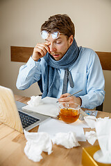 Image showing Feeling sick and tired. Frustrated young man massaging his head while sitting at his working place in office