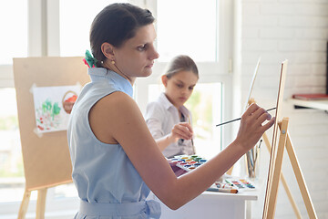 Image showing Artist teaches children to draw on an easel in the studio