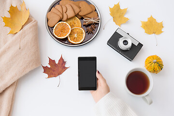 Image showing hand with smartphone, tea and autumn leaves