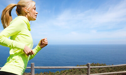 Image showing woman with earphones running at seaside