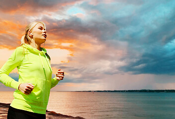 Image showing woman with earphones running over sea sunset