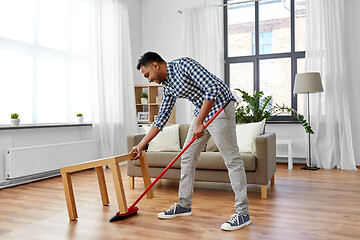 Image showing man with broom cleaning floor under table at home