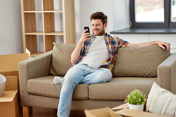 Image showing man with smartphone and boxes on sofa at new home