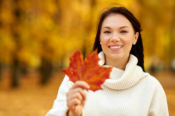 Image showing happy young woman with maple leaf in autumn park