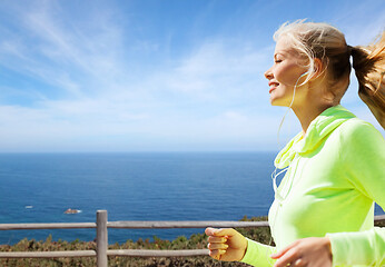 Image showing woman with earphones running at seaside