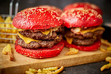 Image showing Set of four homemade giant double becon cheese burgers. Served with french fries on wooden board.