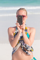 Image showing Beautiful caucasian woman taking a photo on tropical beach summer vacations using her cell phone.