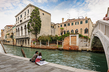 Image showing Venice, Italy. Romainic couple sitting at canal\'s sidewalk close to bridge in historic part of the city