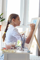 Image showing Girl in white shirt draws behind easel with right hand