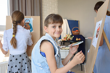 Image showing Girl smiles sitting at easel with paints in the studio