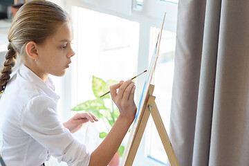 Image showing girl with great interest paints on easel