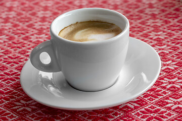 Image showing White cup of coffee with foam and bubbles on a red tablecloth