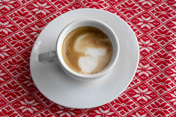 Image showing White cup of coffee with foam and bubbles on a red tablecloth